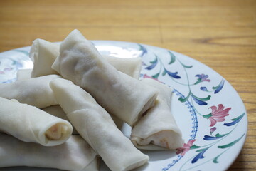 Heap of raw spring rolls(lumpia) on the plate. Frozen food on wooden tables.
