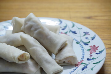Heap of raw spring rolls(lumpia) on the plate. Frozen food on wooden tables.