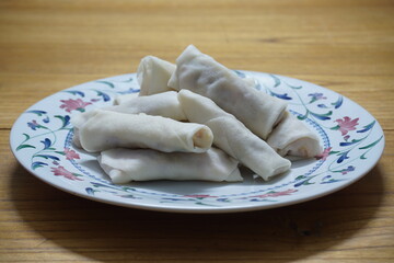 Heap of raw spring rolls(lumpia) on the plate. Frozen food on wooden tables.
