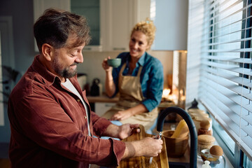 Happy man cleaning wooden cutting board after preparing food in kitchen.