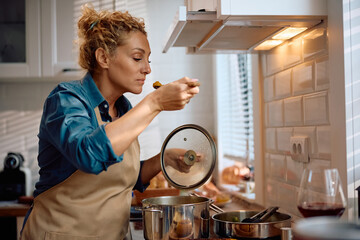 Mid adult woman tasting food while cooking for Thanksgiving in kitchen.