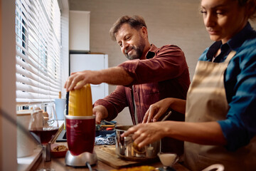 Smiling man using blender while cooking for Thanksgiving meal with his wife in kitchen.