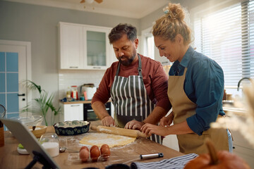 Smiling couple cooperating while baking in kitchen.