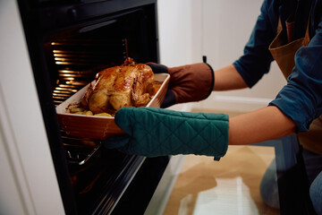 Close up of woman taking roast turkey out of oven.