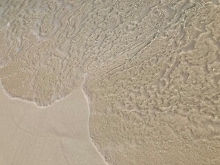 The clear sea waves crashing against the brown sandy beach create patterns look like brain coral