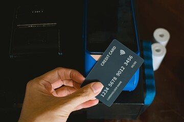 A hand making contactless payment using a black credit card on an EDC card reader machine
