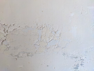 The once smooth white wall now shows signs of wear, with patches of paint peeling away due to moisture seeping in over time.