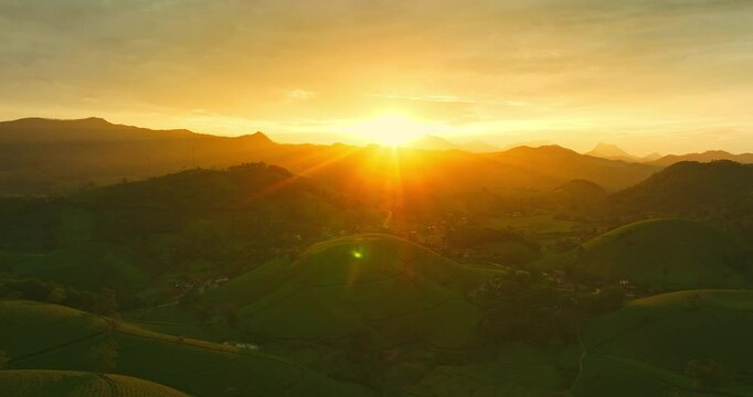 A breathtaking sunrise illuminates the rolling green hills with golden light, casting a warm glow across the lush landscape and distant mountains. This serene scene captures the tranquility of nature 