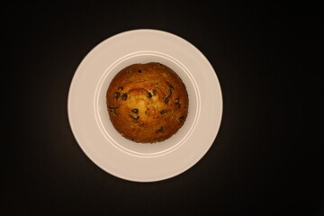 delicious muffin with chocolate chips on a white plate, black background