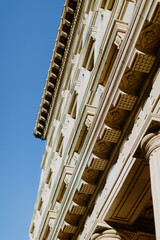 Elegant Neoclassical Facade with Ornate Columns and Intricate Cornices - Low-angle view of neoclassical architecture with detailed columns and ornate cornices against a clear blue sky
