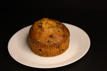 delicious muffin with chocolate chips on a white plate, black background