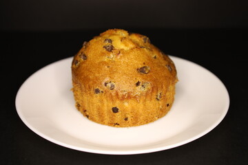 delicious muffin with chocolate chips on a white plate, black background