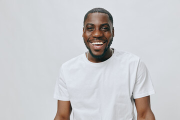 Happy smiling young man wearing a plain white t shirt against a light gray background, expressing...