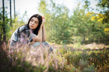 Obraz premium A young woman sitting thoughtfully in a serene forest clearing surrounded by colorful wildflowers on a sunny day