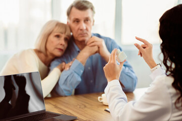 Obraz premium Bad Diagnosis. Female doctor showing pills to scared patients, talking about treatment, free space