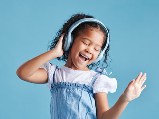 Studio, kid and singing with headphones for dancing, hearing and happy with sound for audio track. Young female person, girl child and listen with technology for music, radio song and blue background