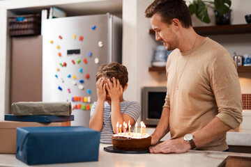 Birthday, dad and child in kitchen, cake and cover of face for surprise, present or growth of youth. Candles, gift and father with son, celebration and single parent with boy, dessert or love in home