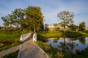Fototapeta premium Park of the 500th Anniversary of Lyuban, Lyuban town (Luban), Leningrad region, Russia. View of pedestrian paths and a bridge near the pond in the city park. Beautiful autumn landscape.