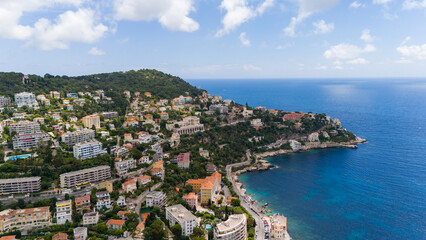 Aerial view of a scenic coastal area in the French Riviera, featuring hillside villas and lush greenery overlooking the clear blue waters of the Mediterranean Sea. Nice, France