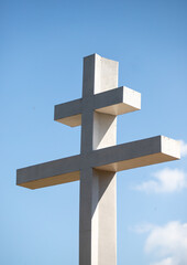 A white cross is standing tall in a blue sky