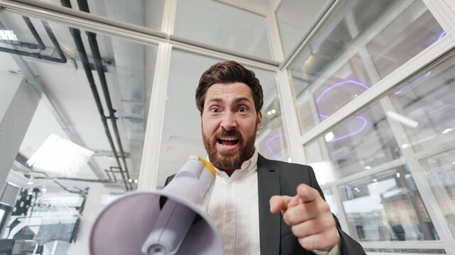Businessman shouting and pointing at the camera through a megaphone. He makes an announcement or shares important information. The man looks surprised.