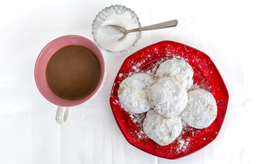 Top view of Kourabiedes, Greek butter cookies, with a cup of coffee and a crystal bowl with sugar and teaspoon, isolated in a white background.