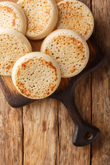 Crumpets fresh from a bakery closeup on the wooden board on the table. Vertical top view from above