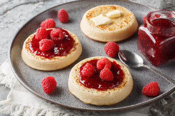 Freshly toasted crumpets on serving dishes with butter, jam and fresh raspberries closeup on the plate on the table. Horizontal