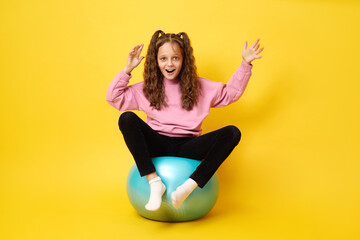 Cute girl with excited expression playing with fitness ball being in playful mood enjoying fun...
