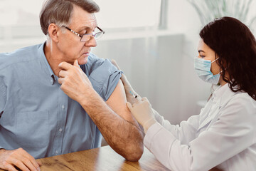 Seasonal Flu Shot. Brazilian nurse in medical mask injecting tetanus toxoid vaccine to senior retired man, copyspace