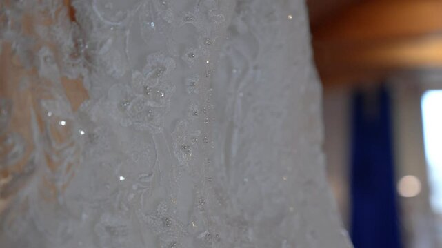 Close-up of white lace wedding dress on hanger, sparkling with sequins and beads