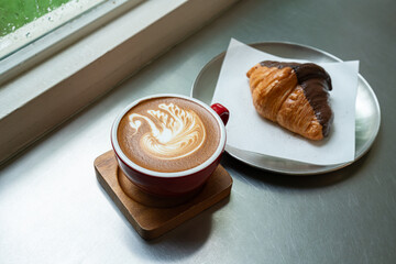 Hot coffee latte with latte art milk foam a swan shape in cup mug with chocolate Croissant on wood desk on top view.As breakfast In a coffee shop at the cafe,during business work concept,Rainy season