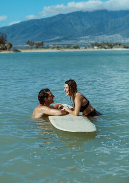 Happy couple in the ocean with surfboard between them