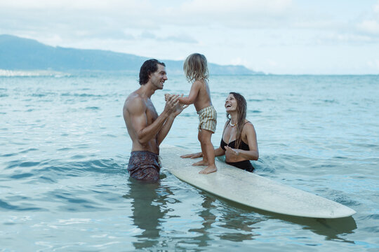 Happy parents helping toddler stand on surfboard