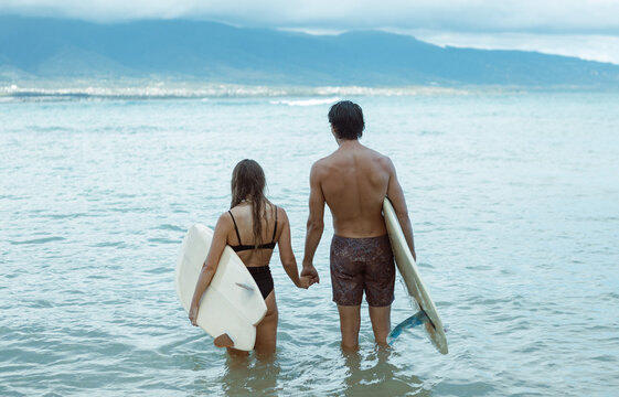Surfer couple holding hands standing in ocean