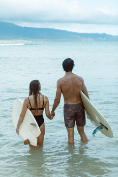 Surfer couple holding hands standing in ocean