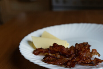 fried bacon and two slices of hard cheese on a white plate