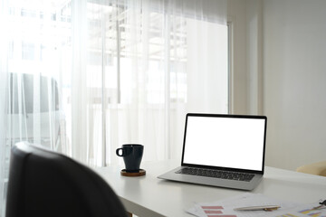 Laptop with blank screen, financial documents and cup of coffee on white table