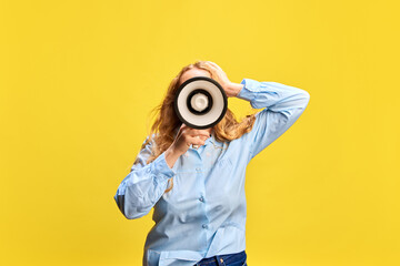 Fototapeta premium Young woman in blue shirt with megaphone against yellow studio background. Seasonal sale Announcement, promotion of weekly specials. Concept of sales, shopping, news, advertisement