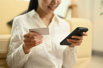 Smiling young Asian woman holding credit card and using mobile phone for online shopping