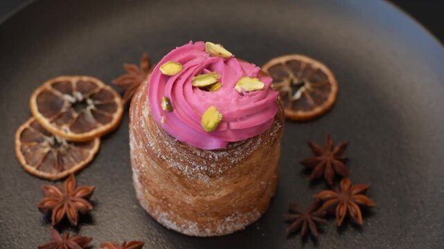 Sweet craffin or panettone garnished with raspberry and pistachio flavored cream on a dark concrete background