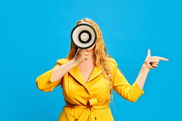 Blonde woman in yellow dress holding megaphone against blue studio background. Retail announcement, flash sales, Black Friday promo. Concept of sales, shopping, news, announcement, advertisement