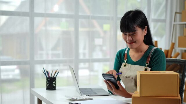 Independent business woman SME uses laptop computer, mobile phone to check customer orders. Checking parcel boxes delivered online at home. Entrepreneur. Freelance. Startup business idea.