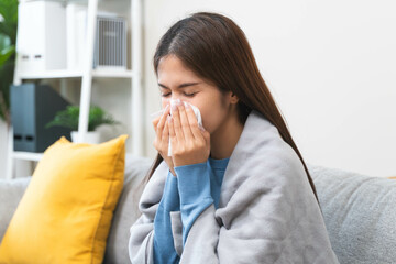 Sick in winter season common cold disease concept, Young woman have a runny nose and flu using tissue to blow her nose on the sofa during winter.