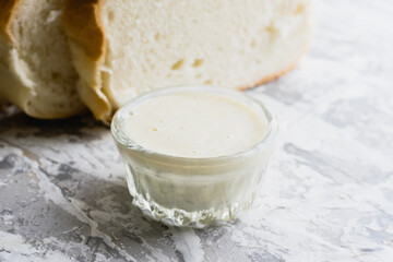 Delicious homemade mayonnaise sauce. Mayonnaise in a glass saucer and appetizing white bread on a light table