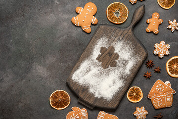 Culinary background with Christmas gingerbread cookies, wooden cutting board with flour, dark grunge background, top view, flat lay, copy space.