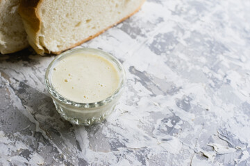 Delicious homemade mayonnaise sauce. Mayonnaise in a glass saucer and appetizing white bread on a light table