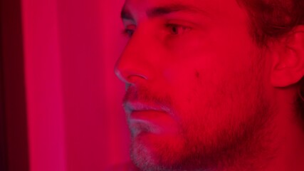 Side profile of man in red lighting, thoughtful expression as he raises head up and nods looking forward, shadows create a dramatic effect