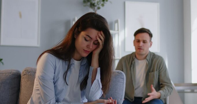 Family couple has troubles, disagreements and conflicts. Tired frustrated bored displeased unhappy angry woman can't forgive adultery, covers holds hand on face, sighs, tries not to listen to husband