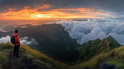 Obraz premium A lone hiker stands on a mountaintop, looking out at a breathtaking sunset over a sea of clouds.